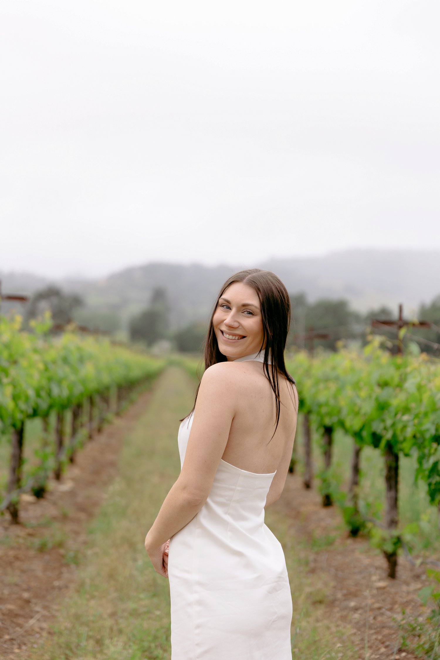 A beautiful smiling bride looking over her shoulder in the vineyards during a Chateau St Jean Winery engagement.