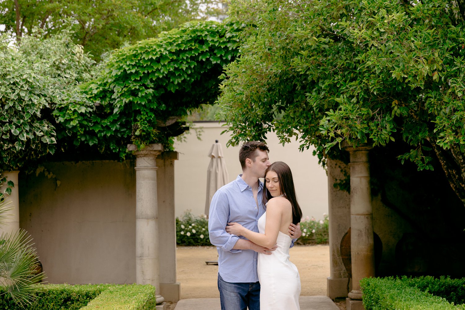A couple holding eachother in front of the beautiful stone arches during a storybook style Chateau St Jean Winery engagement.