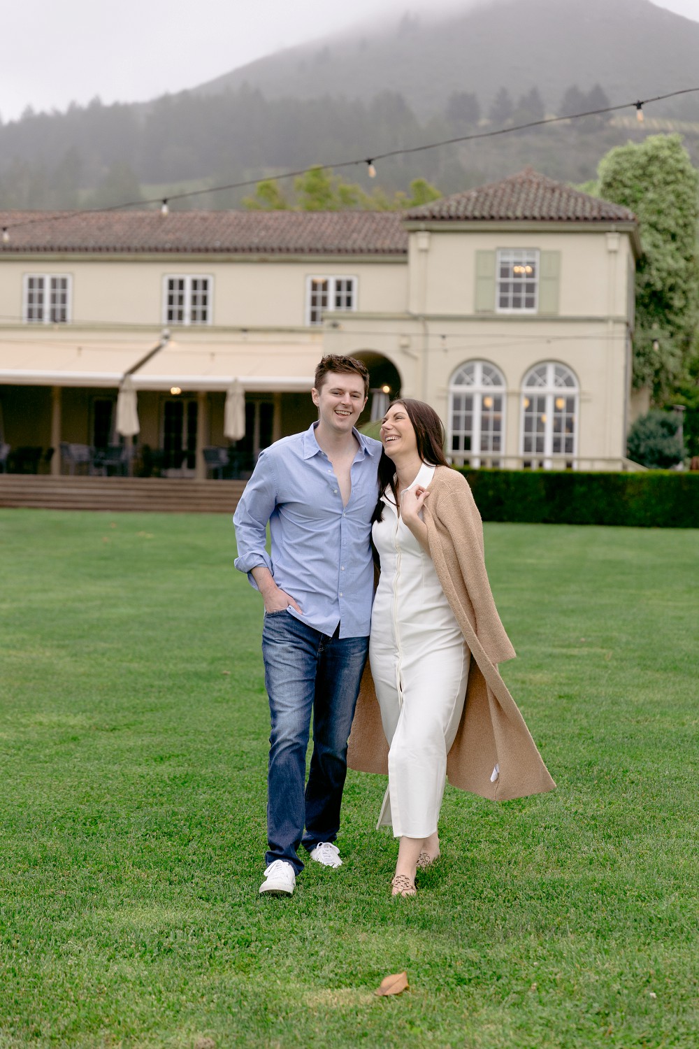 A romantic couple holding hands during their Chateau St Jean Winery engagement session in front of the historic stone estate.